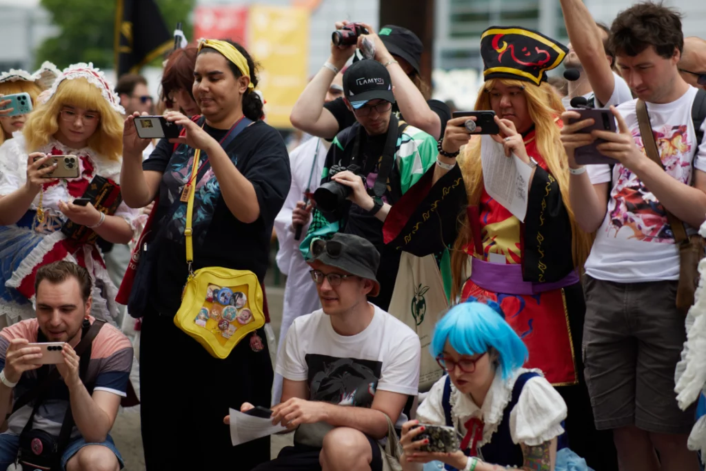 Eine Gruppe, einige davon im Cosplay, fotografieren etwas außerhalb des Bildschirms