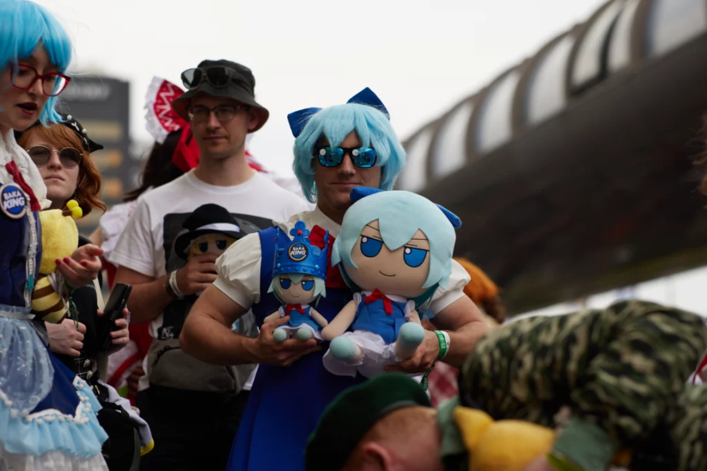 Ein Cirno-Cosplayer hält zwei Cirno-Fumos und schaut in die Kamera